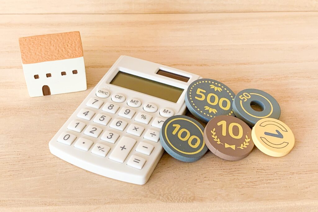 お金を模した木製のコインと電卓と家の形の小物